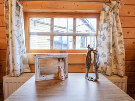 A wooden table under a window with animal patterned curtains and decorative items including a white framed mirror and a metal frog sculpture at Enchanted Cottage in Snettisham