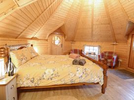 A bedroom with a wooden bed with floral bedding a wooden door two plaid armchairs and a small window at Enchanted Cottage in Snettisham