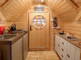 A small wooden kitchen with a sink stove and kettle on the left and cabinets with bread and jars on the right at Enchanted Cottage in Snettisham