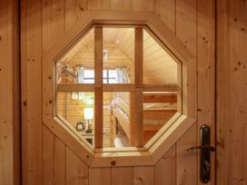 A wooden door with an octagonal glass window looking into a room with bunk beds a nightstand with a lamp and clock and a window with curtains at Enchanted Cottage in Snettisham