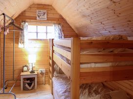 A wooden bunk bed next to a small table with a lamp and clock in a wood-paneled room at Enchanted Cottage in Snettisham