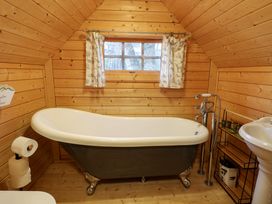 A bathroom with a clawfoot bathtub a small window with curtains wooden walls and floor at Enchanted Cottage in Snettisham