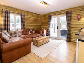 A living room with brown leather sofas a wooden coffee table and checkered curtains at Rabbit Warren Lodge in Snettisham