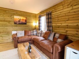 A living room with a brown leather sofa and plaid cushions beside a window with plaid curtains at Rabbit Warren Lodge in Snettisham