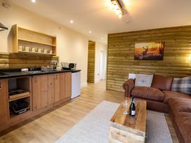 A kitchen and living area with wooden cabinets a brown sofa a wooden coffee table with wine glasses and a bottle on it and a painting of a deer on the wall at Rabbit Warren Lodge in Snettisham