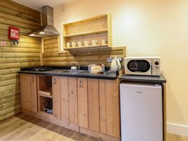 A kitchen with wooden cabinets a stove sink kettle microwave and small refrigerator at Rabbit Warren Lodge in Snettisham