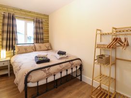 A bedroom with a bed linens with deer designs a wooden side table lamp curtains and a wooden shelving unit with hangers at Rabbit Warren Lodge in Snettisham