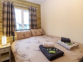 A bedroom with a double bed with deer print bedding beside a window with plaid curtains at Rabbit Warren Lodge in Snettisham