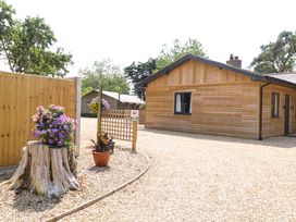 An outdoor view of a wooden house with a garden and gravel path at Rabbit Warren Lodge in Snettisham