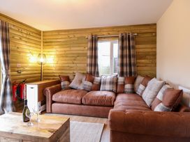 A corner sofa with cushions in a wooden paneled room with a wooden table and wine glasses at Robins Nest Lodge in Snettisham