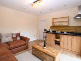 A living area with a brown sofa wooden coffee table and a kitchenette with wooden cabinets at Robins Nest Lodge in Snettisham