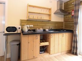 A kitchen with wooden cabinets a microwave kettle sink stove and a trash bin at Robins Nest Lodge in Snettisham