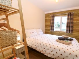 A bedroom with a bed with bird printed bedding a wooden open wardrobe with baskets and a window with plaid curtains at Robins Nest Lodge in Snettisham
