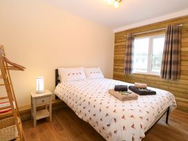 A bedroom with a double bed covered in bird patterned bedding a wooden wall with plaid curtains a side table with a lamp and a wooden clothes rack at Robins Nest Lodge in Snettisham