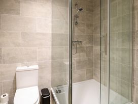A bathroom with a toilet a trash bin a shower with glass doors and tiled walls at Robins Nest Lodge in Snettisham