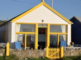 A small white house with yellow window frames and a yellow gated fence with blue striped chairs outside at Homestead in Aberdesach near Penygroes