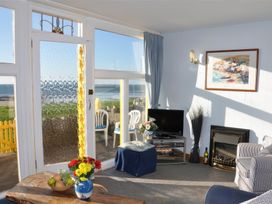 A living room with a glass door and windows overlooking the sea at Homestead in Aberdesach near Penygroes