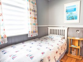 A bedroom with a single bed with nautical bedcover next to a window and a wooden bedside table with a lamp at Homestead in Aberdesach near Penygroes
