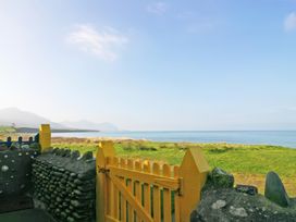 A yellow wooden gate with stone walls overlooking green grass and the sea at Homestead Aberdesach near Penygroes