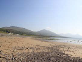 A sandy and rocky beach with mountains and houses in the background at Homestead in Aberdesach near Penygroes
