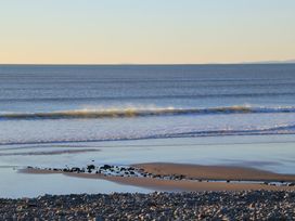 A pebble beach with small waves and distant islands at Homestead in Aberdesach near Penygroes