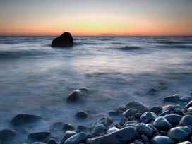 A rocky shoreline with waves and a large rock in the ocean at sunset