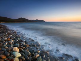 A rocky beach with waves and hills in the background during sunset at Homestead in Aberdesach near Penygroes