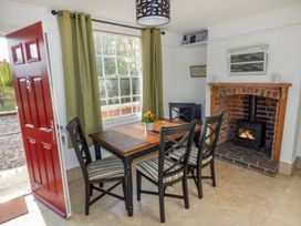 A dining area with a wooden table and four chairs near a window with green curtains and a red door beside a fireplace at 1 Willow Cottage in Upton Upon Severn