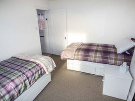 A bedroom with two single beds with plaid bedcovers a white bedside table with tissues and a door open to a hallway at 1 Willow Cottage in Upton Upon Severn