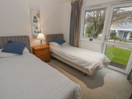 A bedroom with two single beds a wooden nightstand with a lamp a window and a door with striped curtains at Pierpont D1 in Norton near Yarmouth