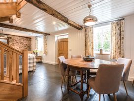 A dining area with a round wooden table and four chairs and a corner with a staircase and a sofa at Tan Llan in Llanelltyd near Dolgellau