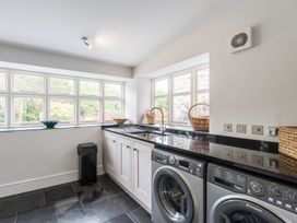 A utility room with a washing machine, dryer, sink, and windows at Tan Llan in Llanelltyd near Dolgellau