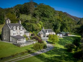 A stone house with multiple chimneys and an adjoining building surrounded by trees and lawn at Tan Llan in Llanelltyd near Dolgellau