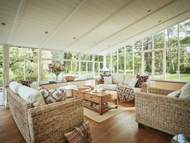A sunroom with wicker sofas a wooden coffee table and large windows showing a garden at Tan Llan in Llanelltyd near Dolgellau