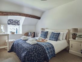 A bedroom with a bed with blue patterned bedding and pillows two bedside tables with lamps a window with floral blinds and a wicker chair at Tan Llan in Llanelltyd near Dolgellau