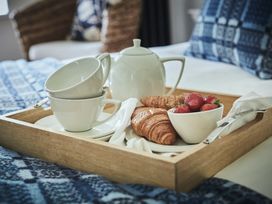 A wooden tray with white teapot two stacked cups croissants and strawberries on a bed with blue patterned blanket at Tan Llan in Llanelltyd near Dolgellau