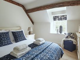 A bedroom with a double bed with patterned blue pillows and bedspread towels on the bed a bedside table with a lamp a window with patterned blinds and decorative vases a blue ottoman with a pillow and blanket at Tan Llan Llanelltyd near Dolgellau