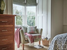 A corner of a bedroom with a plaid armchair next to a window and a wooden chest of drawers at Tan Llan in Llanelltyd near Dolgellau