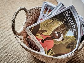 A woven basket holding several magazines on a carpeted floor at Tan Llan in Llanelltyd near Dolgellau