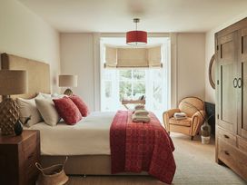 A bedroom with a bed with red pillows and blanket two lamps a wooden wardrobe an armchair and a window at Tan Llan in Llanelltyd near Dolgellau