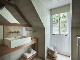 A bathroom with a rectangular sink on a wooden countertop a large mirror and a window with a view of greenery at Tan Llan Llanelltyd near Dolgellau