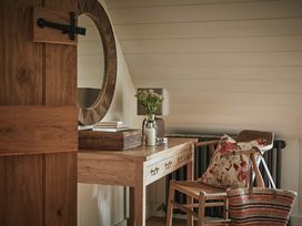 A wooden desk with a round mirror above it and a chair with a floral cushion next to a woven bag at Tan Llan in Llanelltyd near Dolgellau