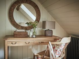 A wooden desk with a round mirror above a lamp flowers basket and chair with cushion at Tan Llan in Llanelltyd near Dolgellau