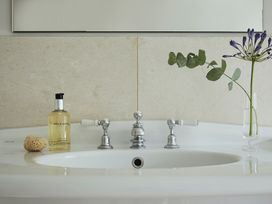 A bathroom sink with chrome faucets a bottle of hand wash a sponge and a flower in a glass vase at Tan Llan in Llanelltyd near Dolgellau