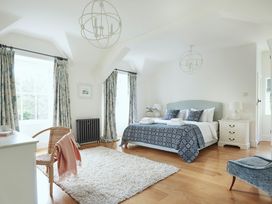 A bedroom with a bed with blue patterned bedding two windows with curtains a white rug a wicker chair and a white nightstand at Tan Llan in Llanelltyd near Dolgellau