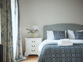 A bedroom with a bed with patterned bedding and pillows next to a white nightstand with a lamp and flowers at Tan Llan in Llanelltyd near Dolgellau