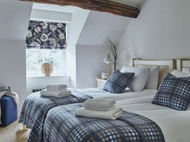 A bedroom with two single beds with blue patterned blankets and pillows a wooden beam and a window with floral blinds at Tan Llan in Llanelltyd near Dolgellau