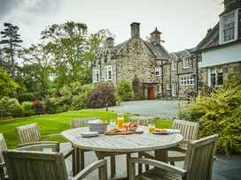 An outdoor patio with a wooden table and chairs set with breakfast items near a stone house surrounded by greenery at Tan Llan in Llanelltyd near Dolgellau