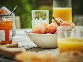 A bowl of peaches on a wooden table with a jar of jam and glasses of orange juice at Tan Llan in Llanelltyd near Dolgellau