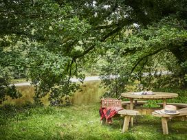 An outdoor wooden picnic table with a picnic basket blanket hats and glasses beside a river under trees at Tan Llan in Llanelltyd near Dolgellau